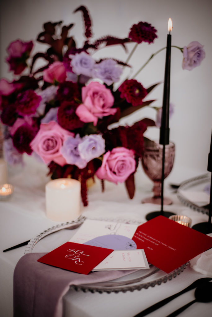 A romantic wedding reception with red and lavender wedding invitations, black candlesticks, and pink and purple wedding flowers.