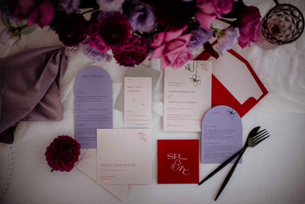 Red and lilac wedding invitation suite with nude coloured card and a flower detail. The inclusion card and wedding menu are an arched shape.