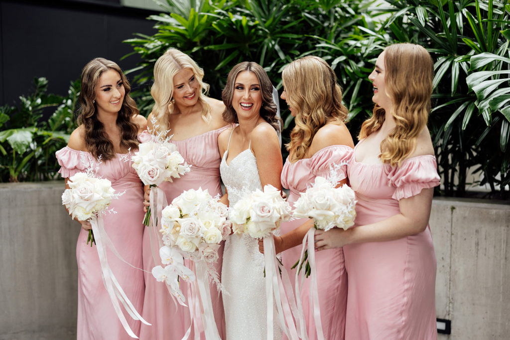 Bride and her bridesmaids, wearing baby pink dresses and holding pink and white bouquets