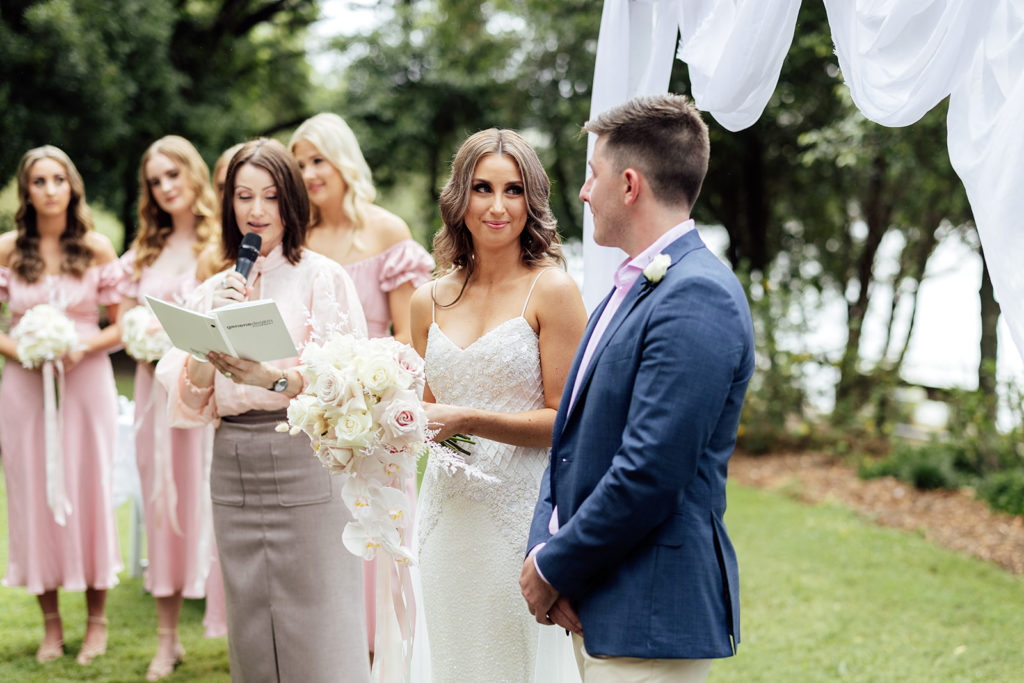 Bride and groom at the altar in a park, with celebrant and bridesmaids in pale pink dresses.