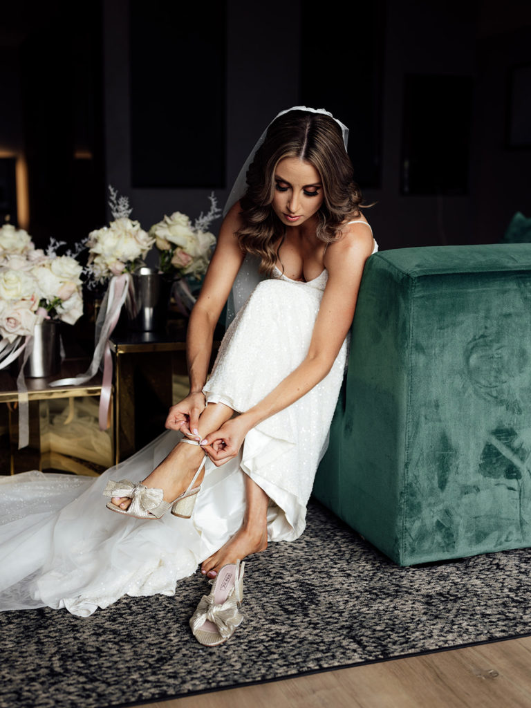 Bride getting ready on her wedding day, sitting down putting on her shoes.