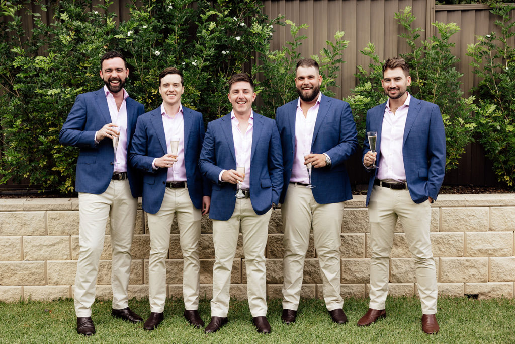 Groom and groomsmen in navy blue suit jackets, sand brown pants, and pale pink shirts