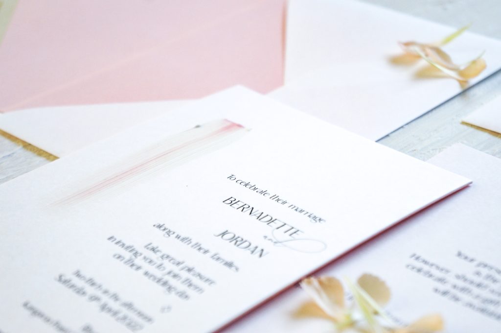 White wedding invitation with minimalist design and painted pink stripe, paired with white envelope and pink envelope liner.