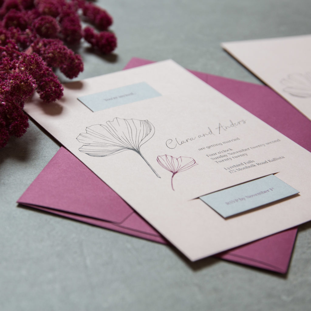 Close up of pink and grey wedding invitations with plum envelope
