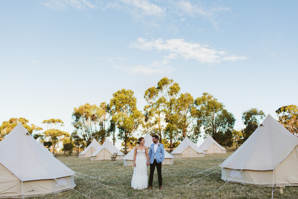 Wedding with a bride and groom standing amongst large white festival-style tents. Caitlin is wedding planner and stylist Paradise Hunter.
