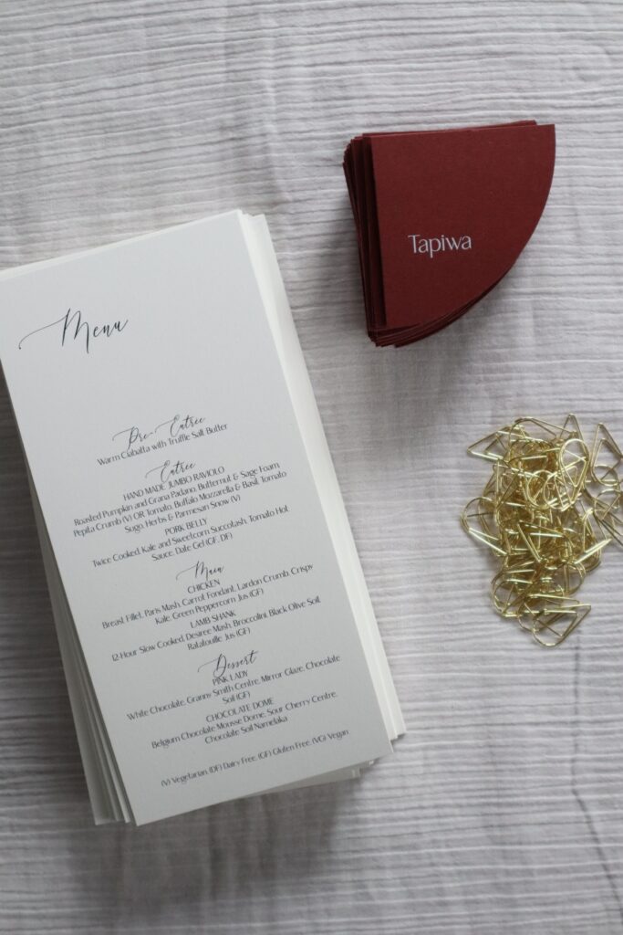 Ivory wedding menus with burgundy place cards and gold teardrop clasps.