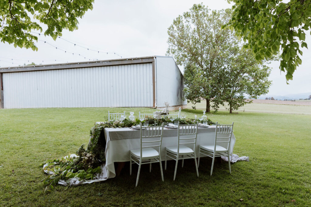 A styled wedding reception table with an industrial hanger and farm in the background