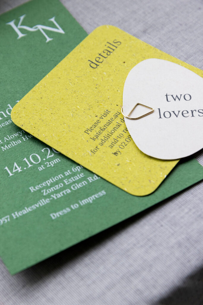 Natural wedding invitations with green card made from grass, and cards held together with a gold clasp.