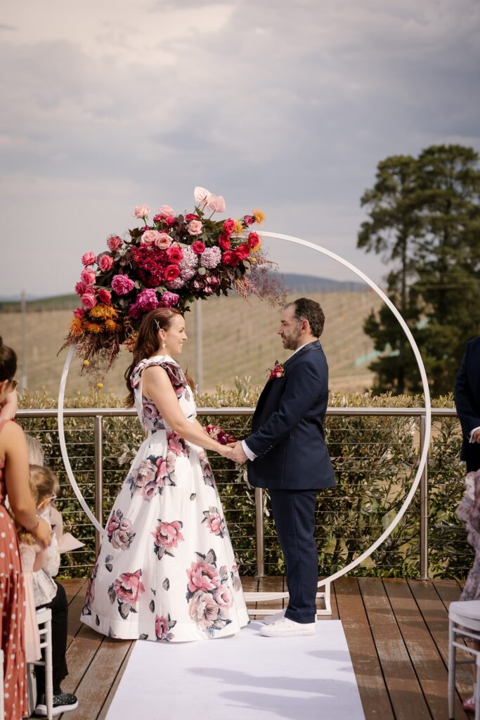 A bride and a groom at the alter in an outdoor wedding with colourful flowers and a floral dress.