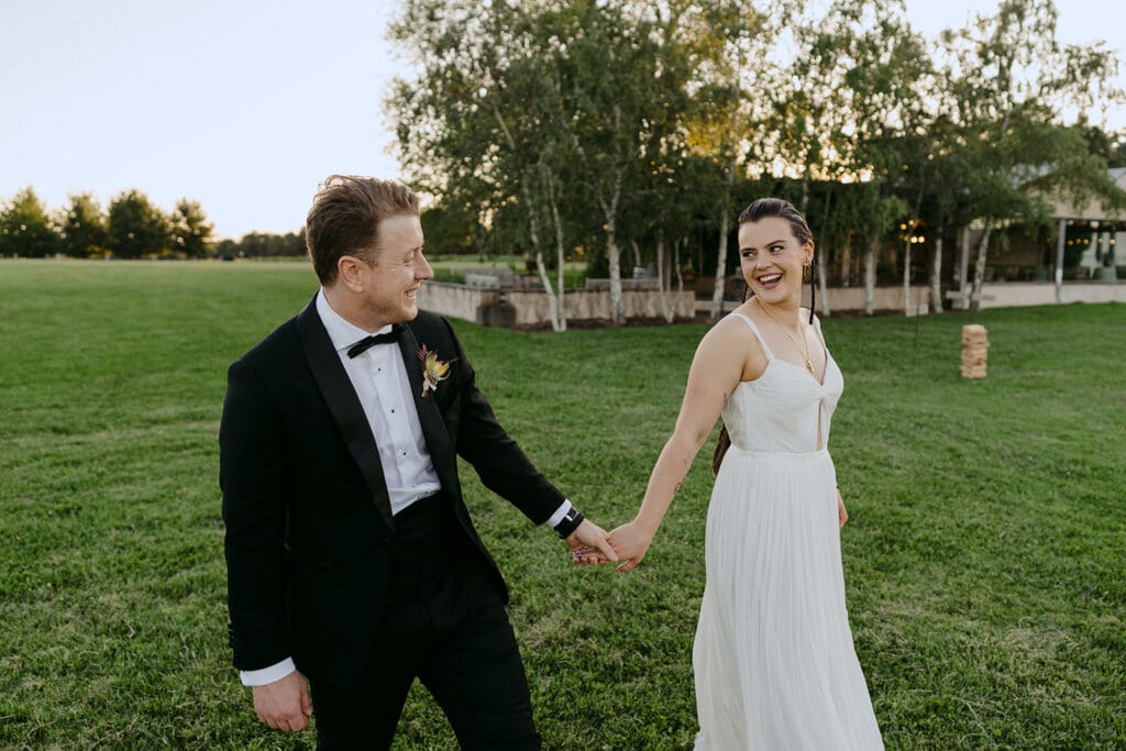 A bride and a groom holding hands walking along the grass