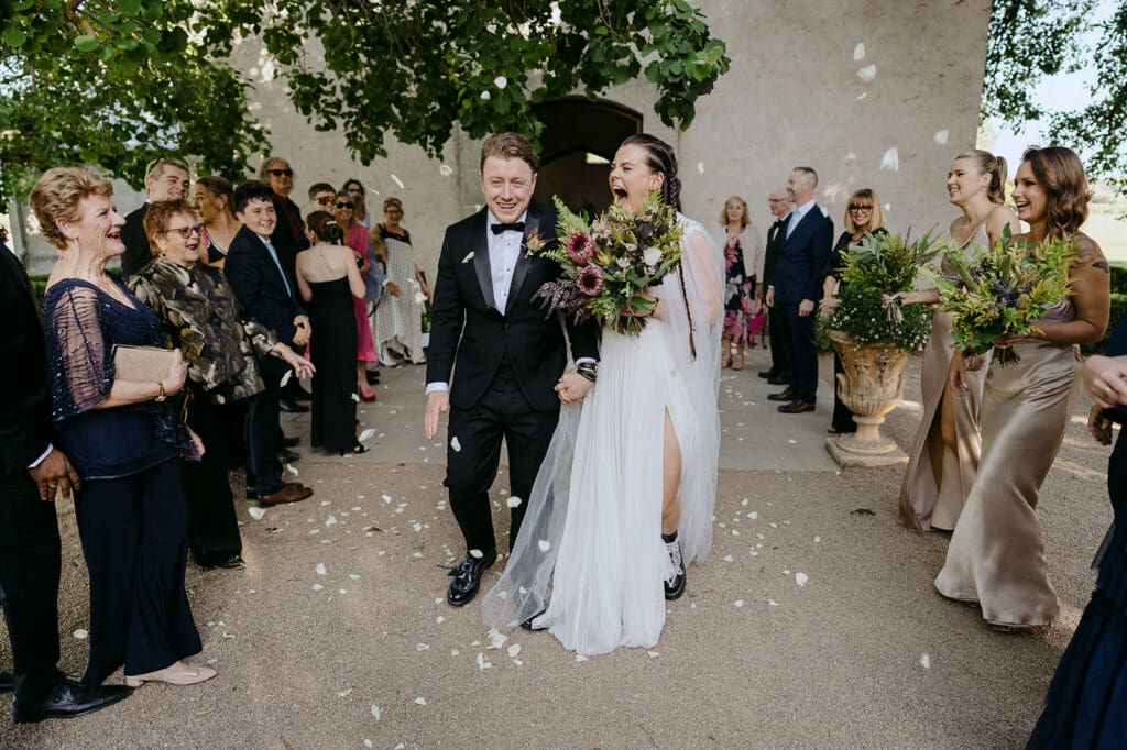 A bride and a groom walking back down the aisle at Stones of the Yarra Valley with guests throwing rose petals.