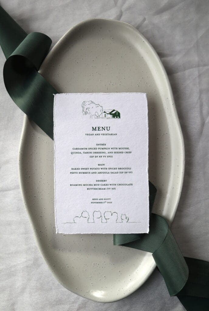 A wedding menu printed on Indie Handmade paper, with dark green text and illustrations.  The menu sits on an ivory platter with sage green ribbon.
