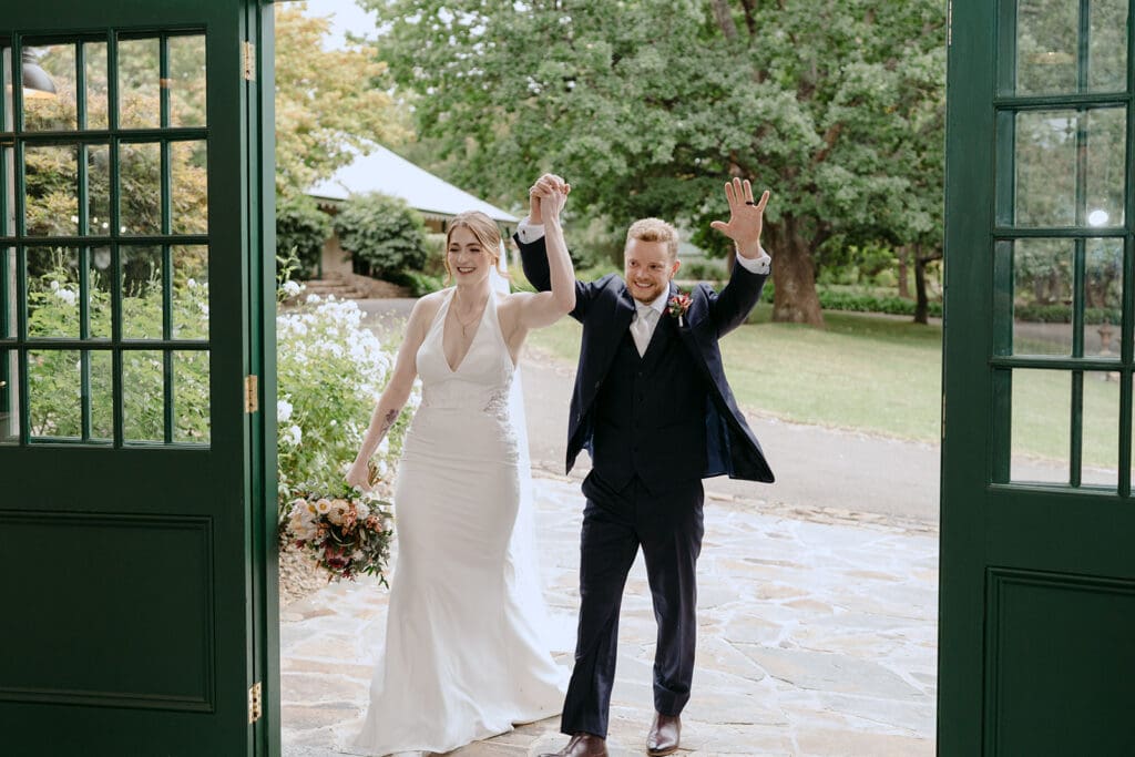 A bride and groom making their first entrance at their wedding reception through the green doors at Flowerdale Estate.