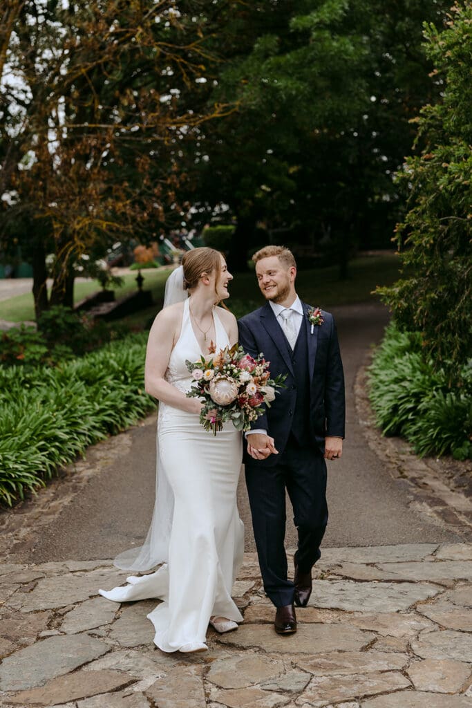 A bride and groom holding hands and holding a bouquet while walking outside at Flowerdale Estate.