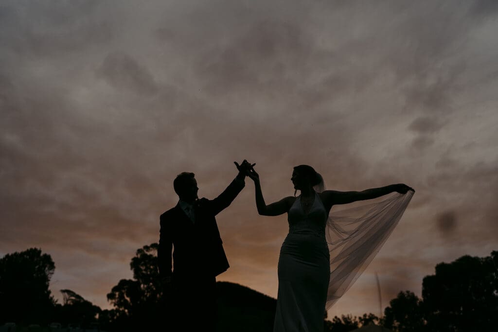 The silhouette of a bride and groom holding hands at sunset.