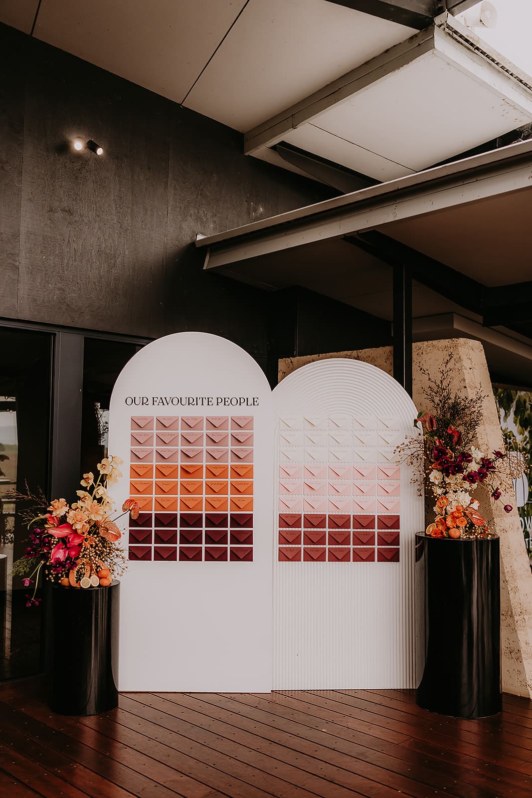 An escort card display on a white backdrop with pink and orange and burgundy envelopes.